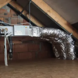 Centrala wentylacyjna z rekuperacją, zamontowana na poddaszu, z widocznymi przewodami wentylacyjnymi w izolacji aluminiowej i elementami instalacji odprowadzającej skropliny.