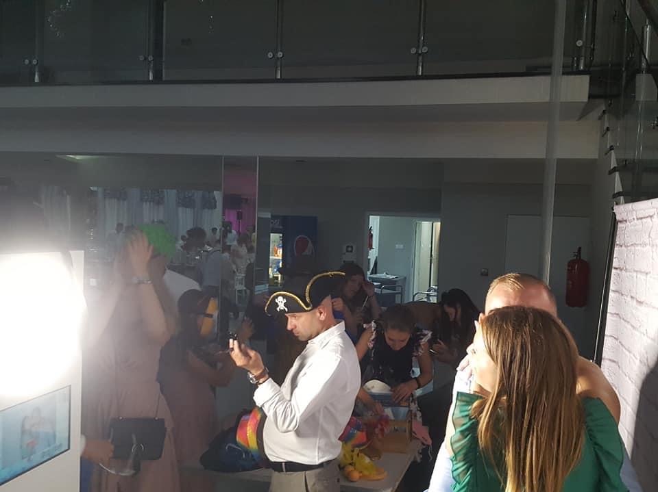 Goście w strojach i perukach korzystają z fotobudki podczas imprezy. Mężczyzna w kapeluszu pirackim robi zdjęcie telefonem.