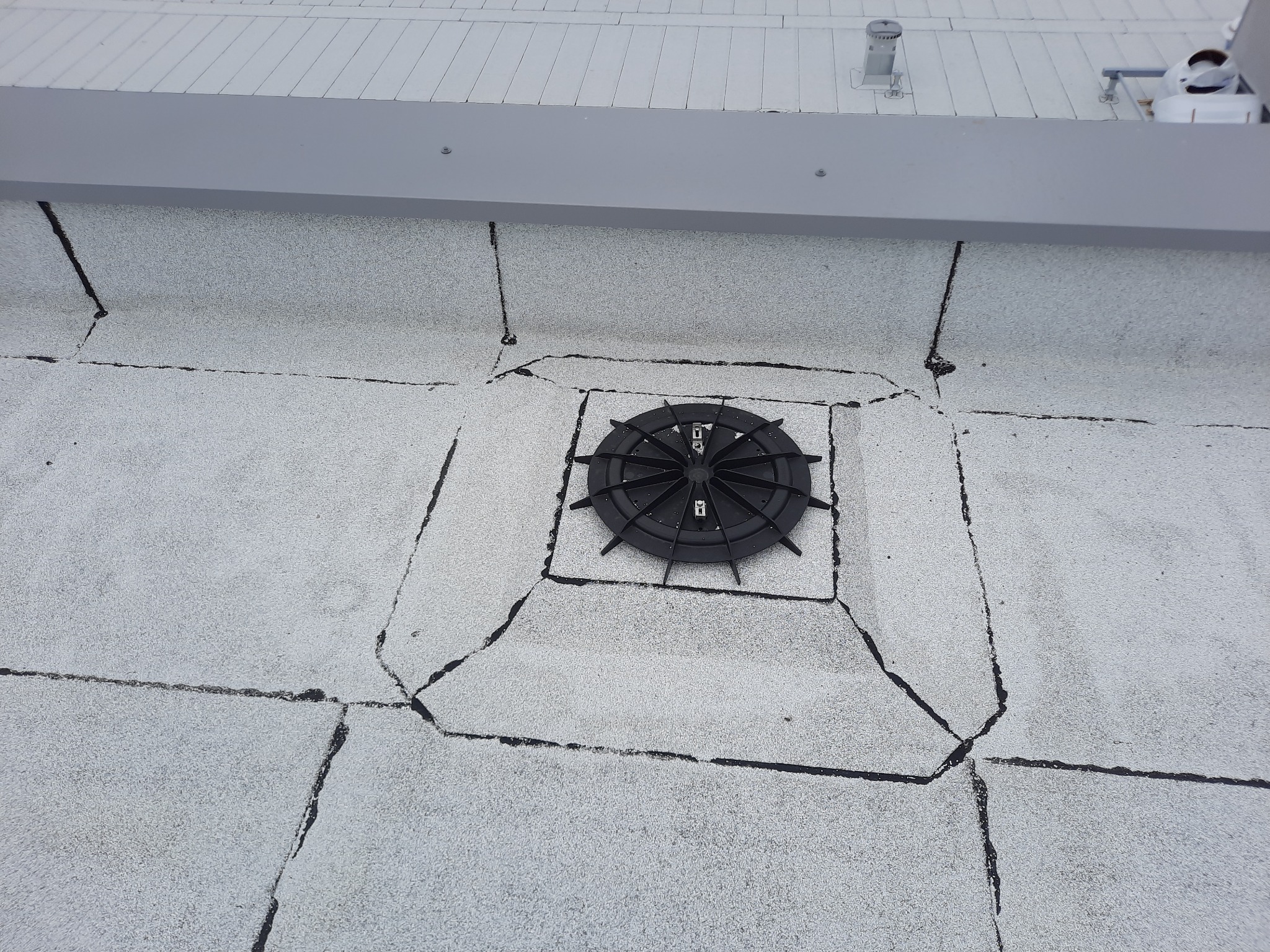 Płaski dach pokryty papą z widocznym wpustem dachowym, otoczonym uszczelnieniami.