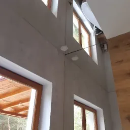 Wysokie okna z drewnianą stolarką w wykończonym wnętrzu domu we Wrocławiu, widoczne szare ściany i fragment drewnianej podłogi oraz armatura łazienkowa.