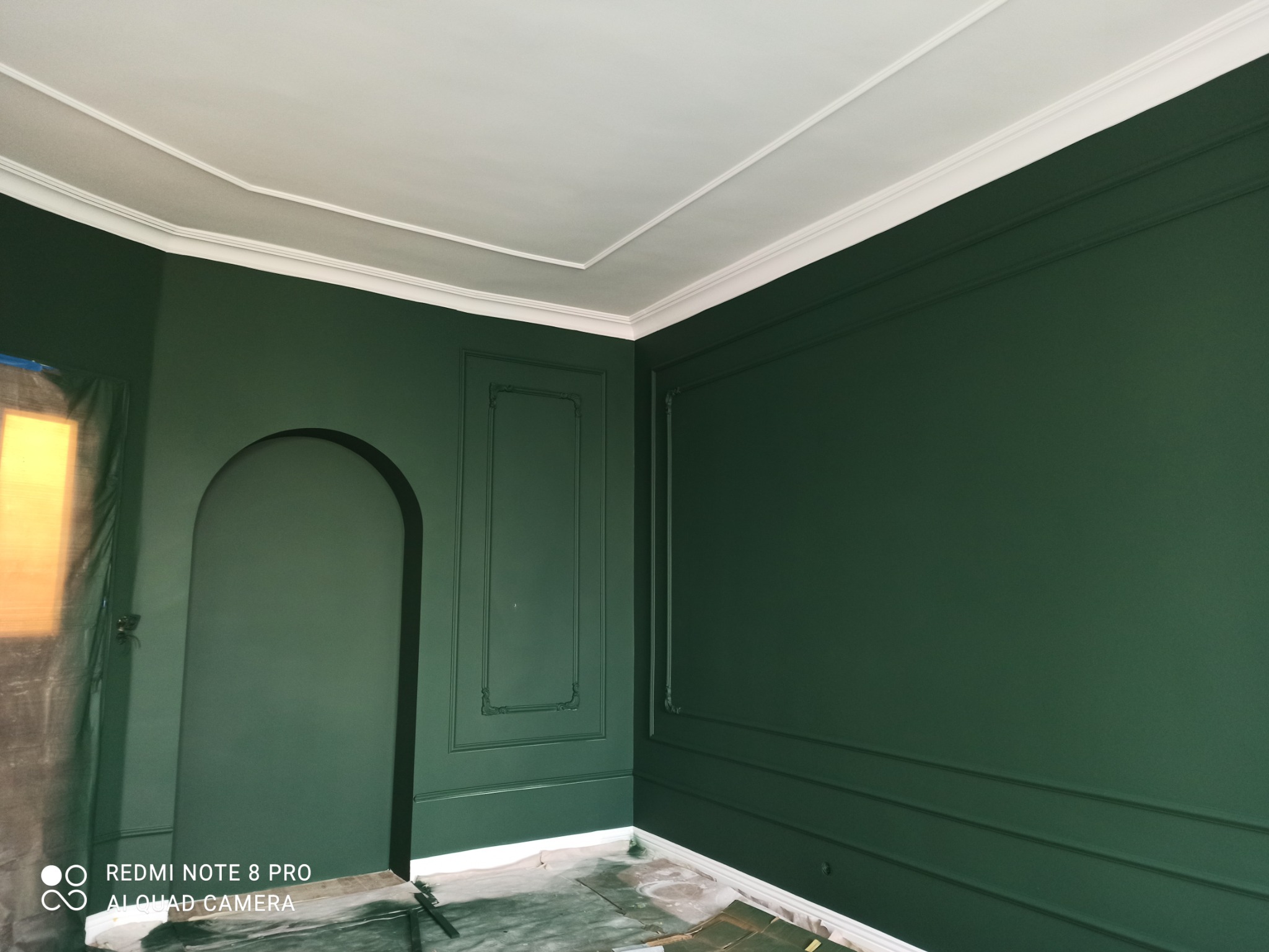Pokój z ciemnozielonymi ścianami i białym sufitem, ozdobne listwy przypodłogowe i sufitowe, przygotowany do dalszych prac wykończeniowych, podłoga zabezpieczona folią.