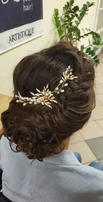 Upięcie włosów z ozdobną, złoto-perłową spinką, widoczne z tyłu głowy, z delikatnym warkoczem i kręconymi kosmykami przy szyi.