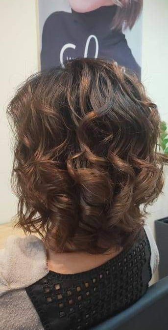 Krótkie, brązowe, kręcone włosy z tyłu głowy, po zabiegu stylizacji, widok na kark i czarną ażurową bluzkę.