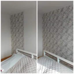 Fragment pokoju z tapetą w roślinny wzór, widok na ścianę nad łóżkiem, gdzie część ściany jest biała, a część pokryta tapetą w odcieniach szarości i beżu.