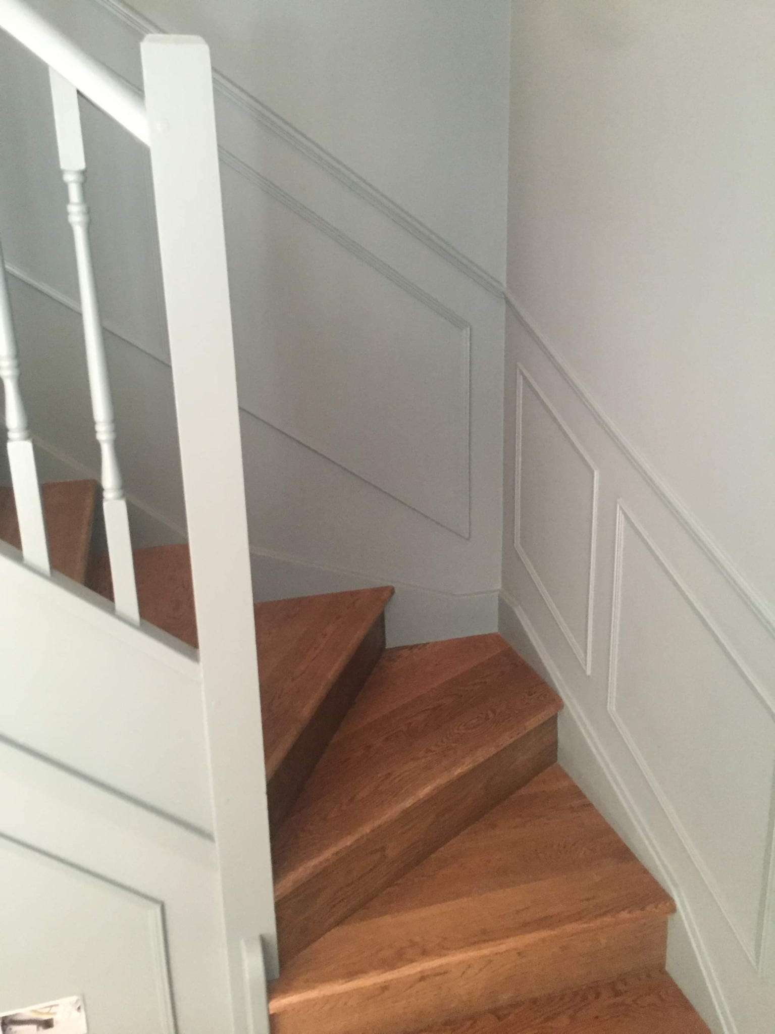 Schody drewniane z pomalowanymi na szaro ścianami z dekoracyjnymi panelami i białą balustradą.