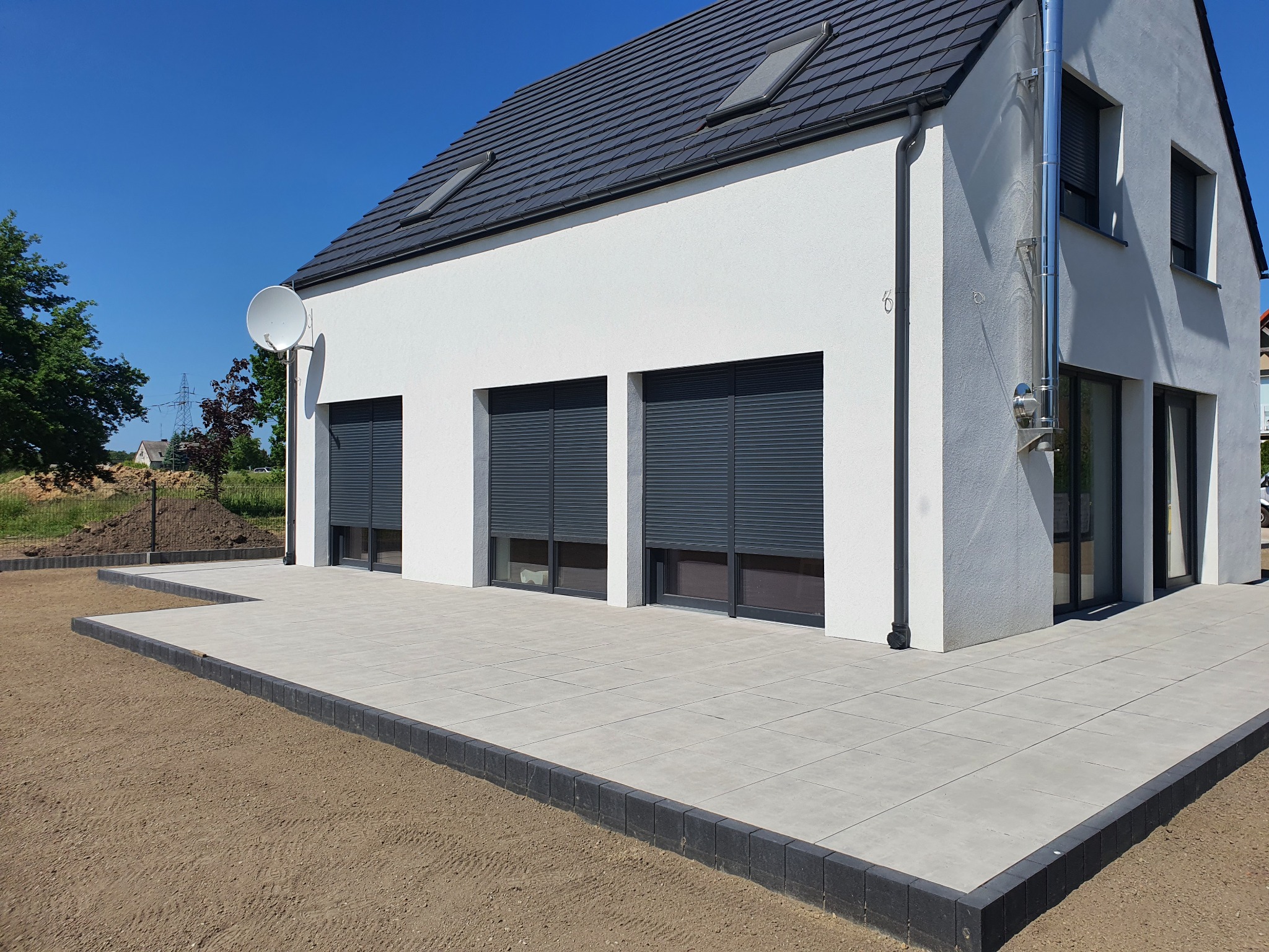 Nowoczesny dom jednorodzinny w Kokoszkowach z utwardzonym terenem wokół, wyłożonym jasnoszarą kostką brukową i obrzeżami z ciemnej kostki.