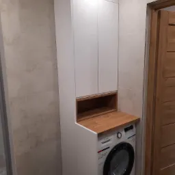 Biała szafa łazienkowa na wymiar z drewnianym blatem nad pralką Bosch, dopasowana do beżowych płytek. Funkcjonalne rozwiązanie w małej łazience.