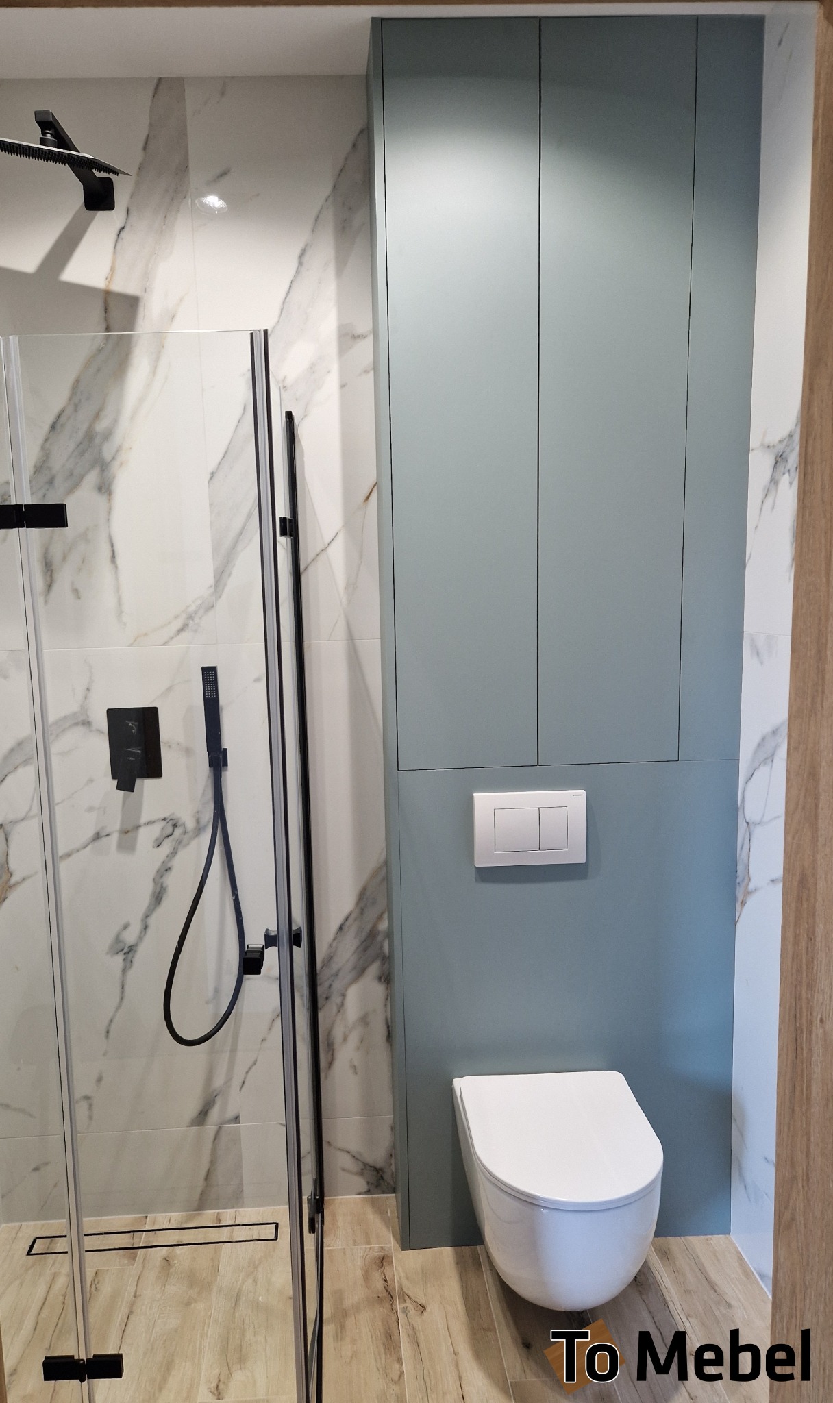 Niebieska szafka wnękowa w łazience z marmurowymi płytkami i czarną armaturą prysznicową. Widoczna toaleta podwieszana i drewnopodobna podłoga.