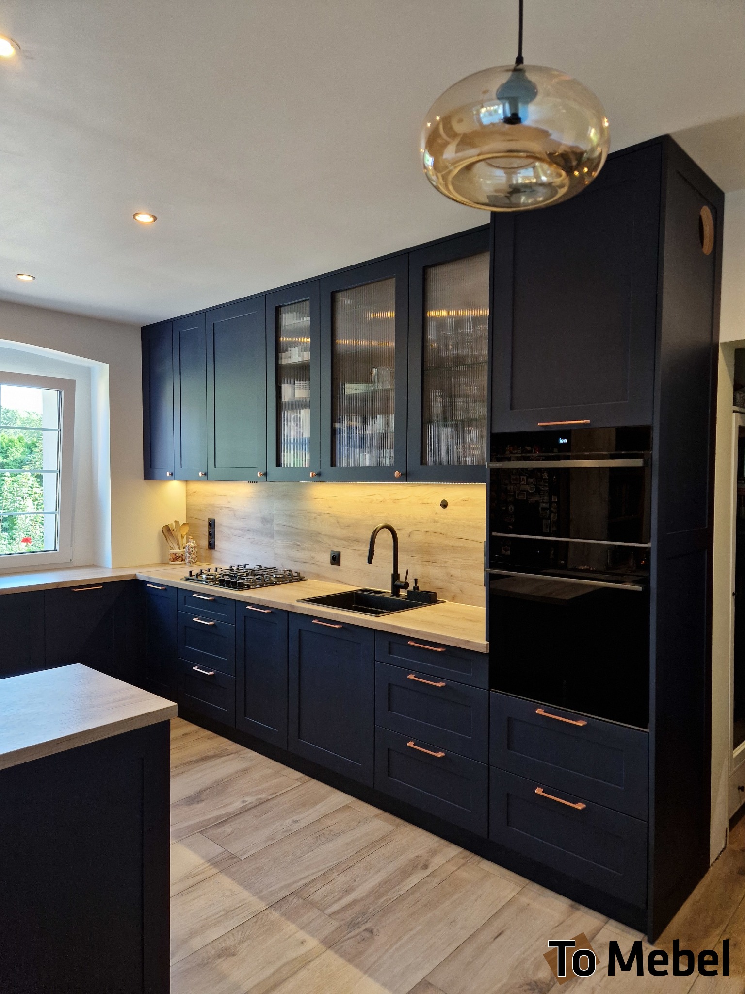 Elegancka, ciemna kuchnia z drewnianymi akcentami: fronty szafek z ryflowanego szkła, miedziane uchwyty, drewniany blat i podłoga. Nowoczesny design z oświetleniem LED.