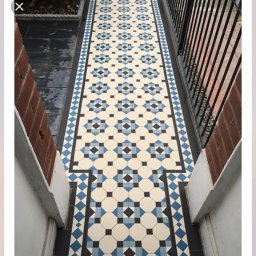 Tomasz Olszewski - Wzorzysta, kremowo-niebiesko-czarna podłoga z płytek w stylu wiktoriańskim, ułożona na wąskim korytarzu w Choszcznie, widok z góry, z elementami muru z czerwonej cegły po bokach.