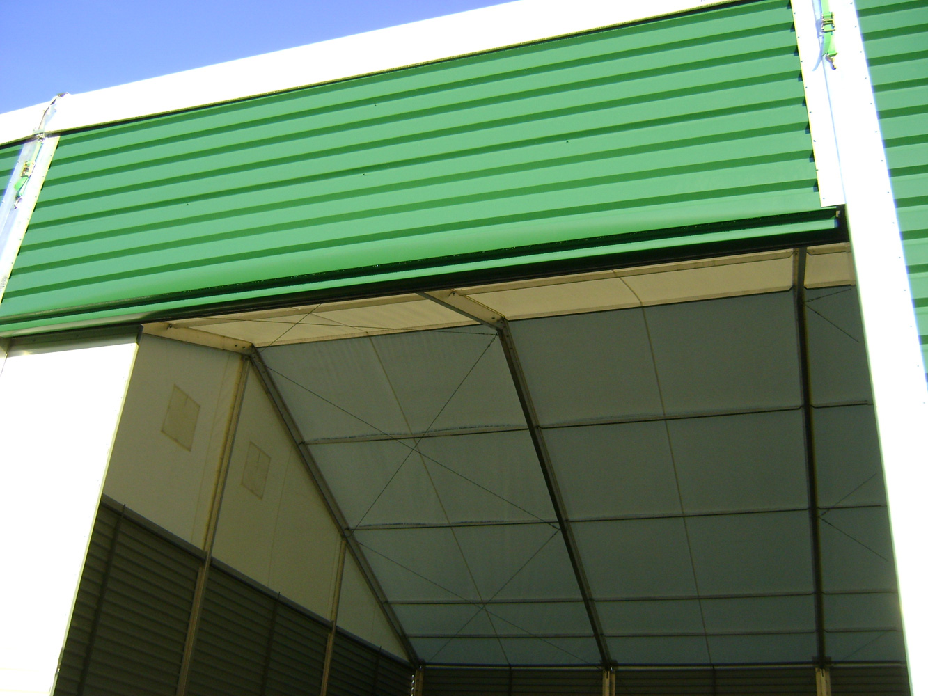 Wnętrze hali namiotowej z zielonymi panelami zewnętrznymi, widok z dołu na konstrukcję dachu i ścian z białego materiału.