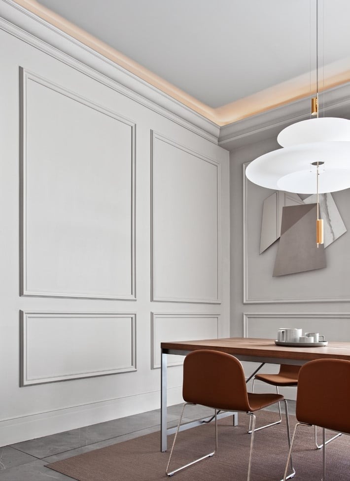 Eleganckie wnętrze jadalni z drewnianym stołem, brązowymi krzesłami i dekoracyjnymi panelami ściennymi w odcieniach szarości, oświetlone nowoczesną lampą wiszącą i listwą LED pod sufitem.