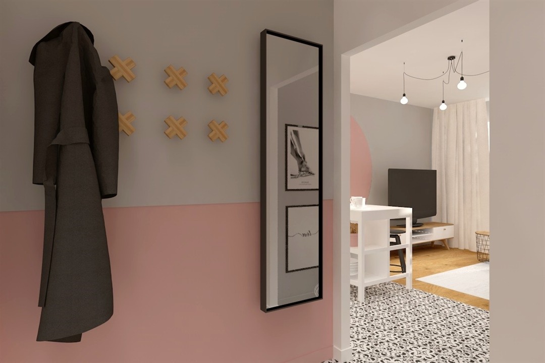 Wnętrze przedpokoju z szaro-różową ścianą, drewnianymi wieszakami krzyżykowymi, wysokim lustrem w czarnej ramie, wieszakiem z płaszczem i widokiem na salon z ażurowym dywanem, białymi meblami...
