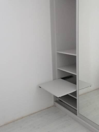 Wnętrze szafy przesuwnej z wysuwanym blatem, widoczne półki i lustrzane drzwi.