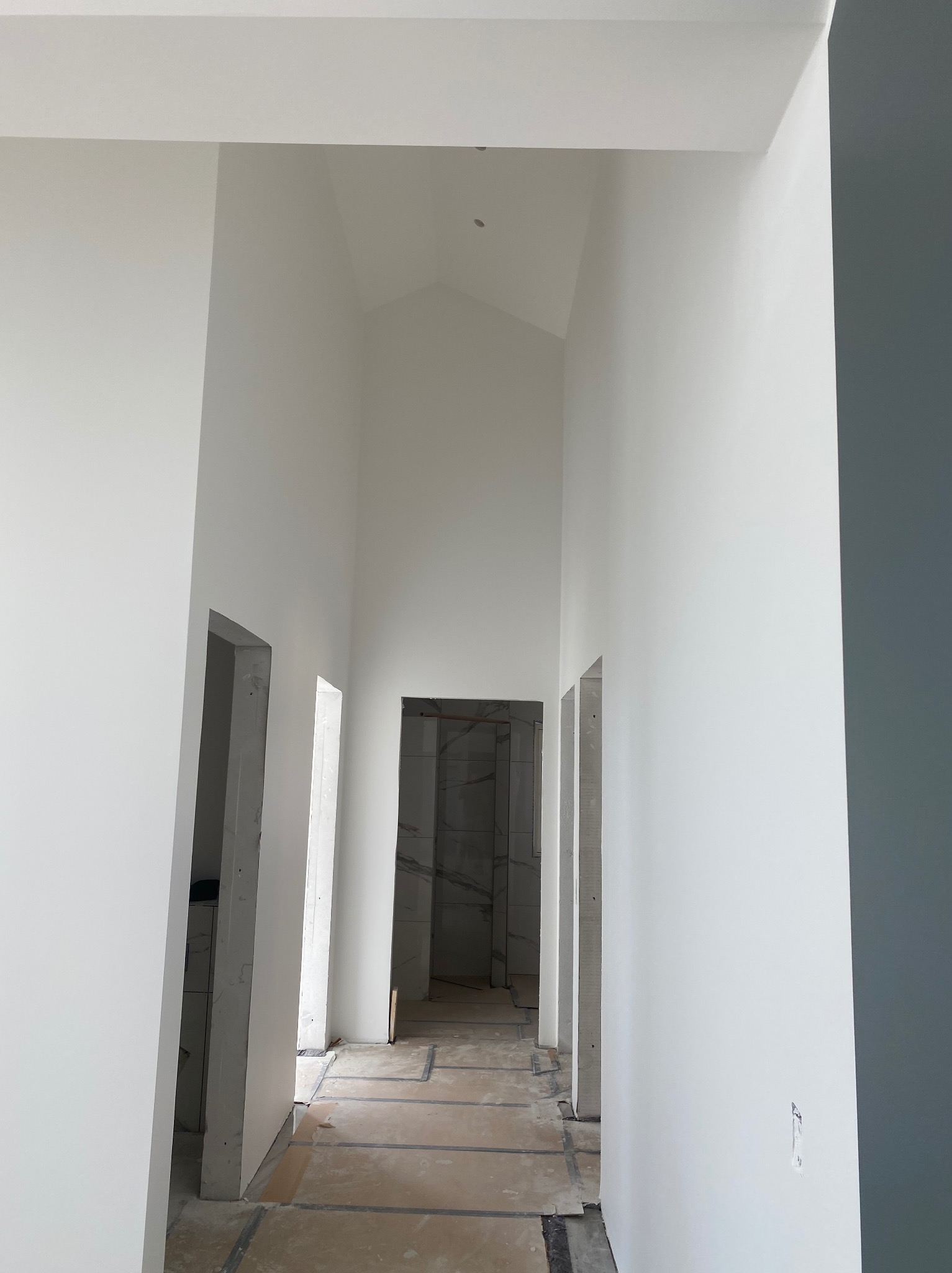 Wnętrze w trakcie remontu: białe ściany, surowe otwory drzwiowe. Widoczne przygotowania do wykończenia podłogi i ścian, surowy stan przed finalnym malowaniem.