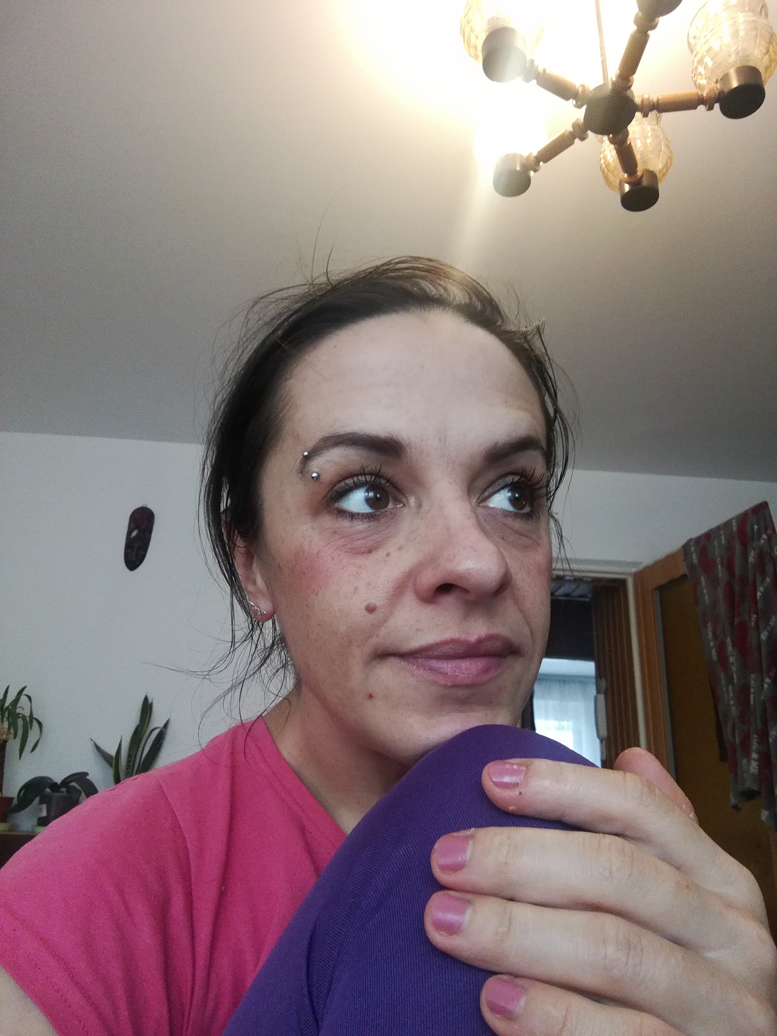 Portret kobiety z kolczykiem w brwi, spoglądającej w górę, w tle widoczny żyrandol i fragment pokoju w Dębicy.