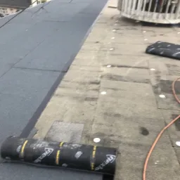 Częściowo pokryty papą dach płaski z widoczną rolką papy Nexler, fragmentem starego pokrycia i elementami wentylacji w tle.