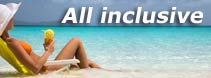 Kobieta w kapeluszu relaksuje się na leżaku na plaży, popijając drinka z widokiem na turkusowe morze, z napisem 'All inclusive' w górnej części kadru.