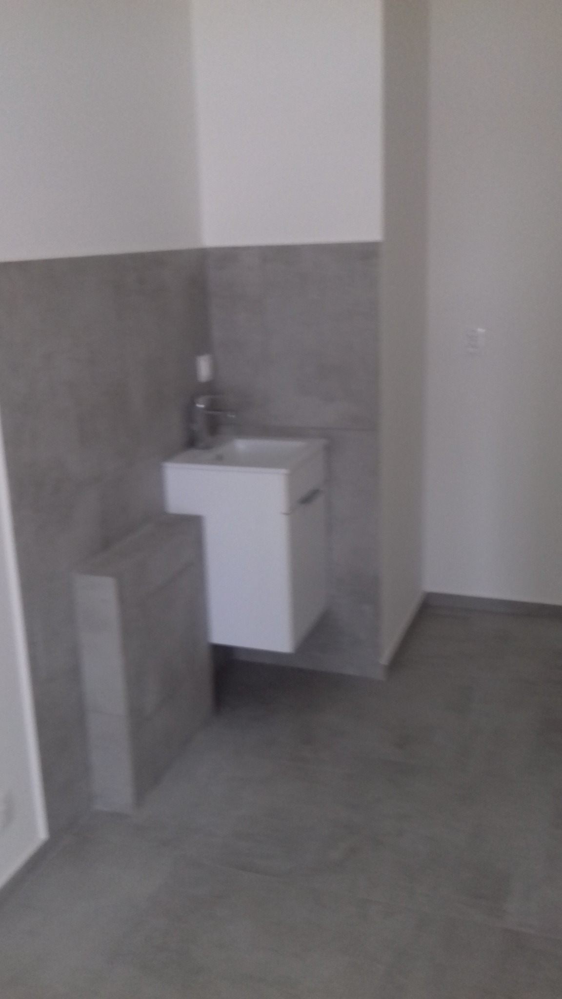 Nowoczesna umywalka wisząca z szafką w łazience wykończonej szarymi płytkami, widoczny fragment podłogi i ściany.