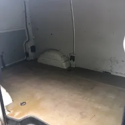 Wnętrze pustego, białego busa z widoczną podłogą z tworzywa i ścianami z blachy, przygotowanego do załadunku.