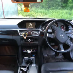 Wnętrze samochodu Mercedes-Benz z widoczną deską rozdzielczą, kierownicą, skórzanymi siedzeniami i zawieszką zapachową o smaku melona na lusterku wstecznym.