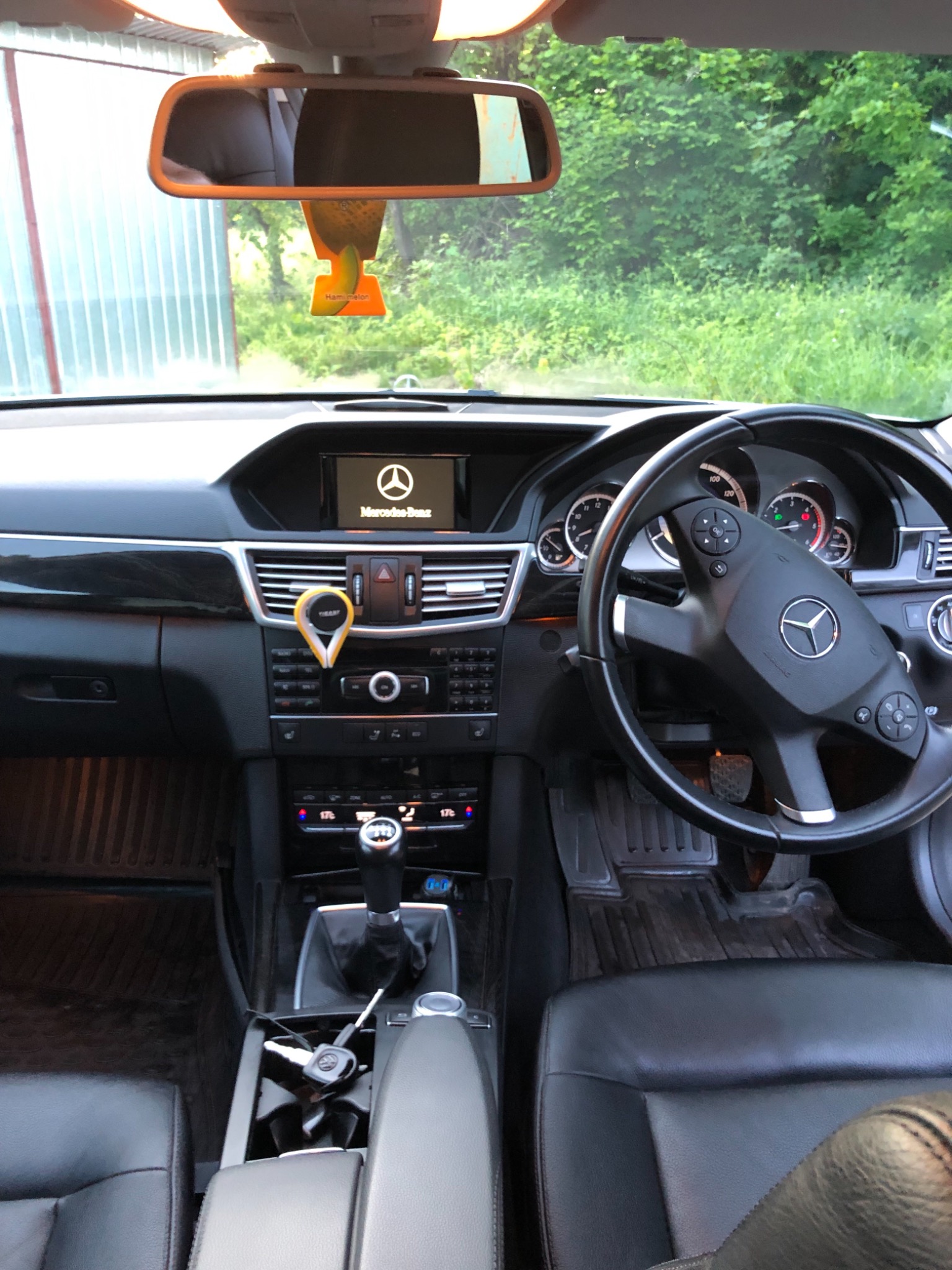 Wnętrze samochodu Mercedes-Benz z widoczną deską rozdzielczą, kierownicą, skórzanymi siedzeniami i zawieszką zapachową o smaku melona na lusterku wstecznym.