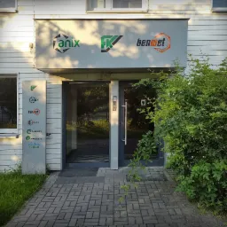 Wejście do budynku z szyldem firm Anix, FK i Benmet oraz tablicą z logo firm.