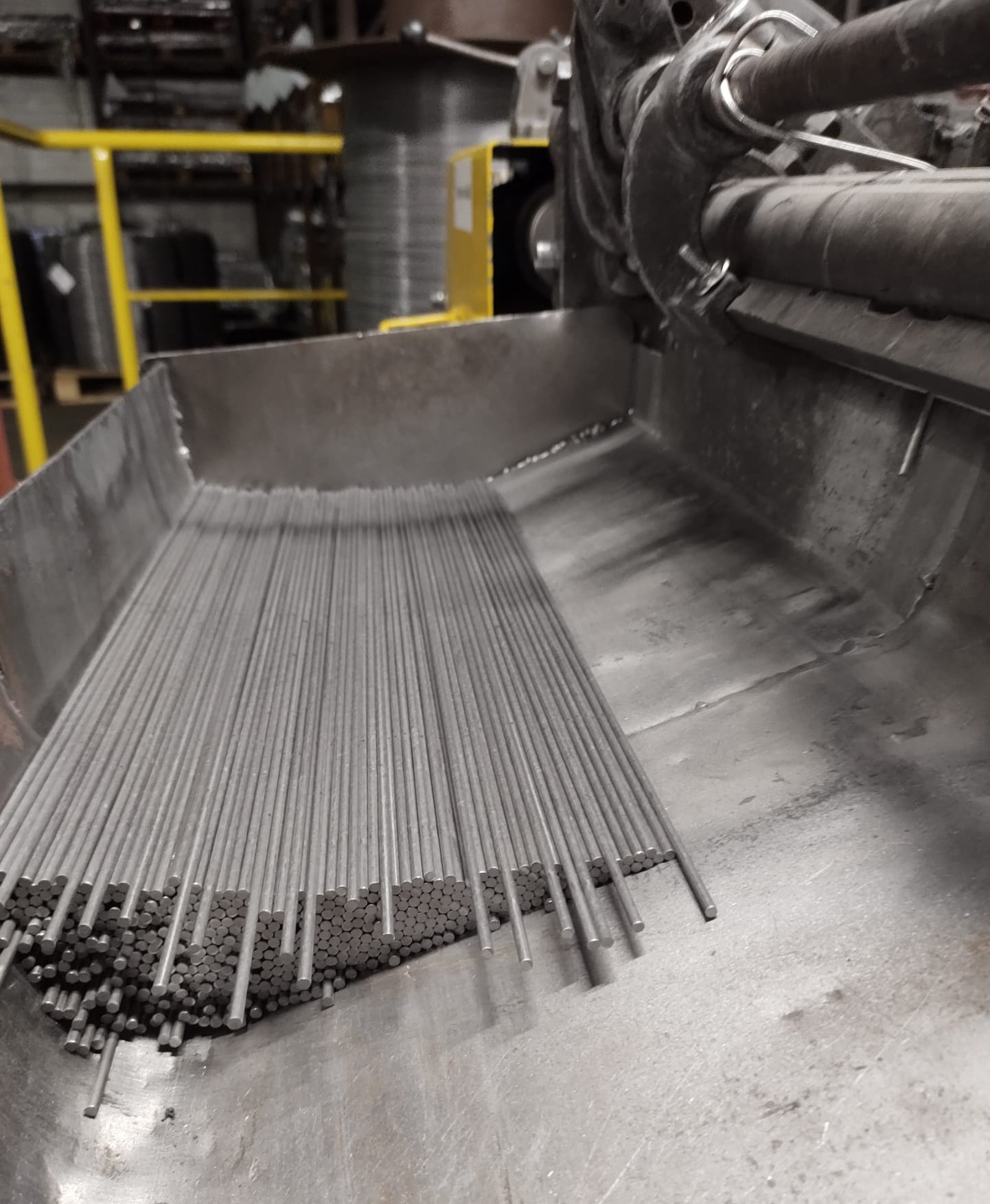 Metalowe pręty wychodzące z maszyny do obróbki metali, ułożone równolegle w metalowej tacy.