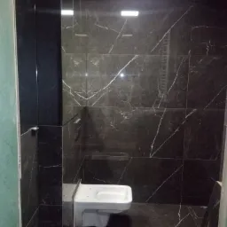 Nowoczesna łazienka z czarnymi płytkami imitującymi marmur i podwieszaną toaletą, widoczne niedokończone prace wykończeniowe przy ścianie.