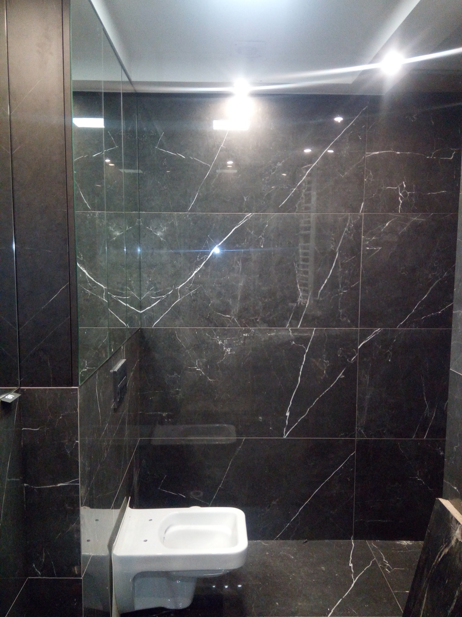 Wykończona łazienka z czarnymi płytkami imitującymi marmur, widoczna toaleta i szklana kabina prysznicowa.