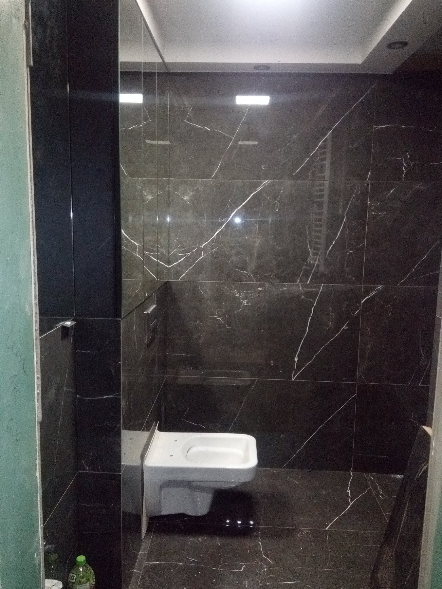 Nowoczesna łazienka z czarnymi płytkami imitującymi marmur i podwieszaną toaletą, widoczne niedokończone prace wykończeniowe przy ścianie.