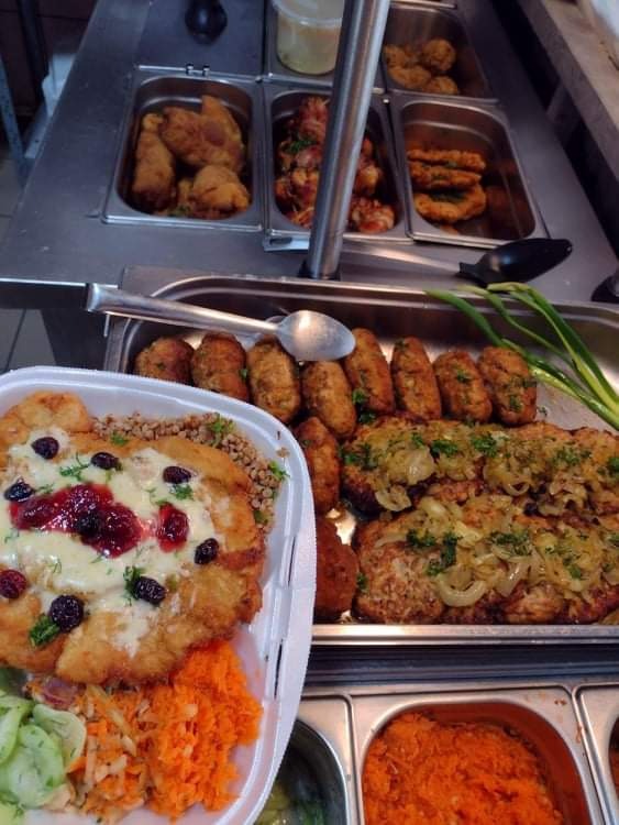 Bufet z różnorodnymi daniami: kotlety z cebulą, krokiety, smażony kurczak, ryba z sosem żurawinowym i sałatki w pojemnikach.