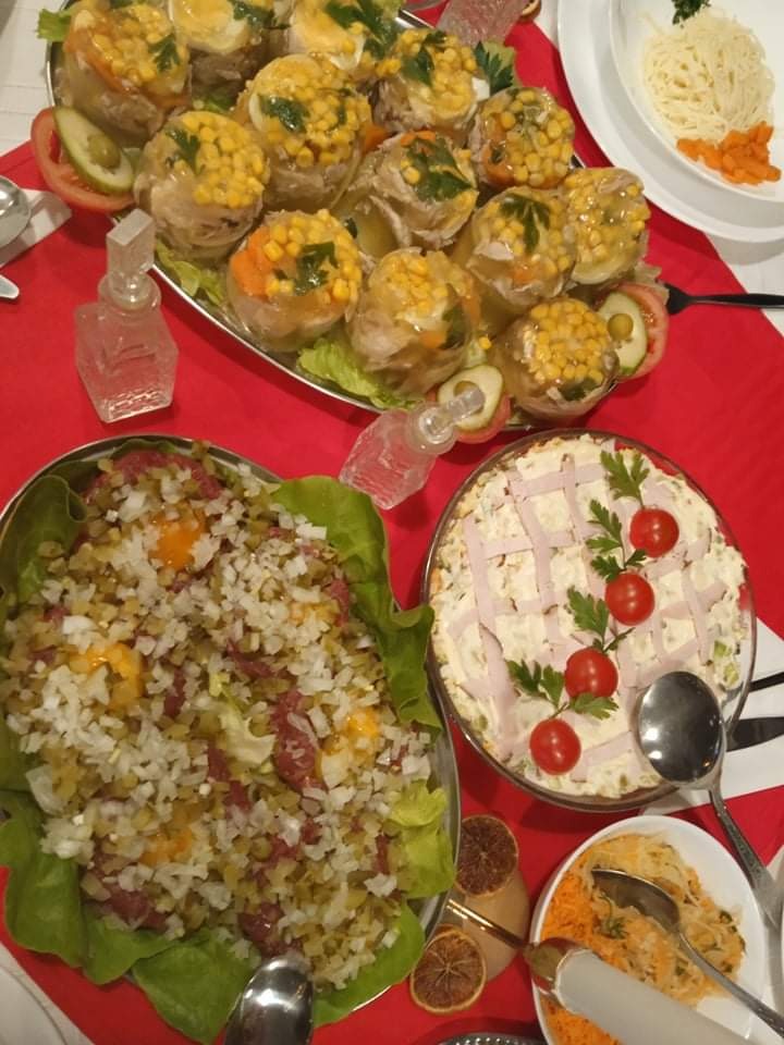 Zimne nóżki z warzywami w galarecie, sałatka jarzynowa z dekoracją z szynki i pomidorków koktajlowych oraz sałatka z jajkiem i ogórkiem na stole z czerwonym obrusem w Łodzi.