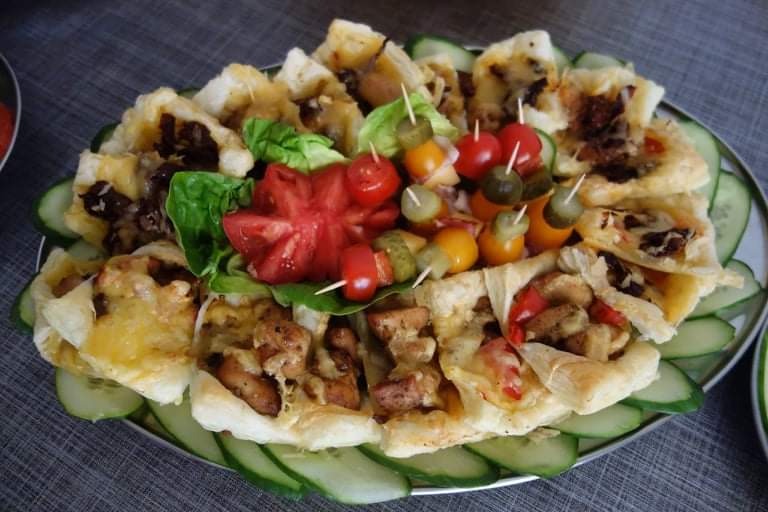 Dekoracyjnie ułożone na srebrnej tacy tartaletki z różnymi farszami, ozdobione ogórkiem, pomidorkami koktajlowymi i korniszonami na wykałaczkach.