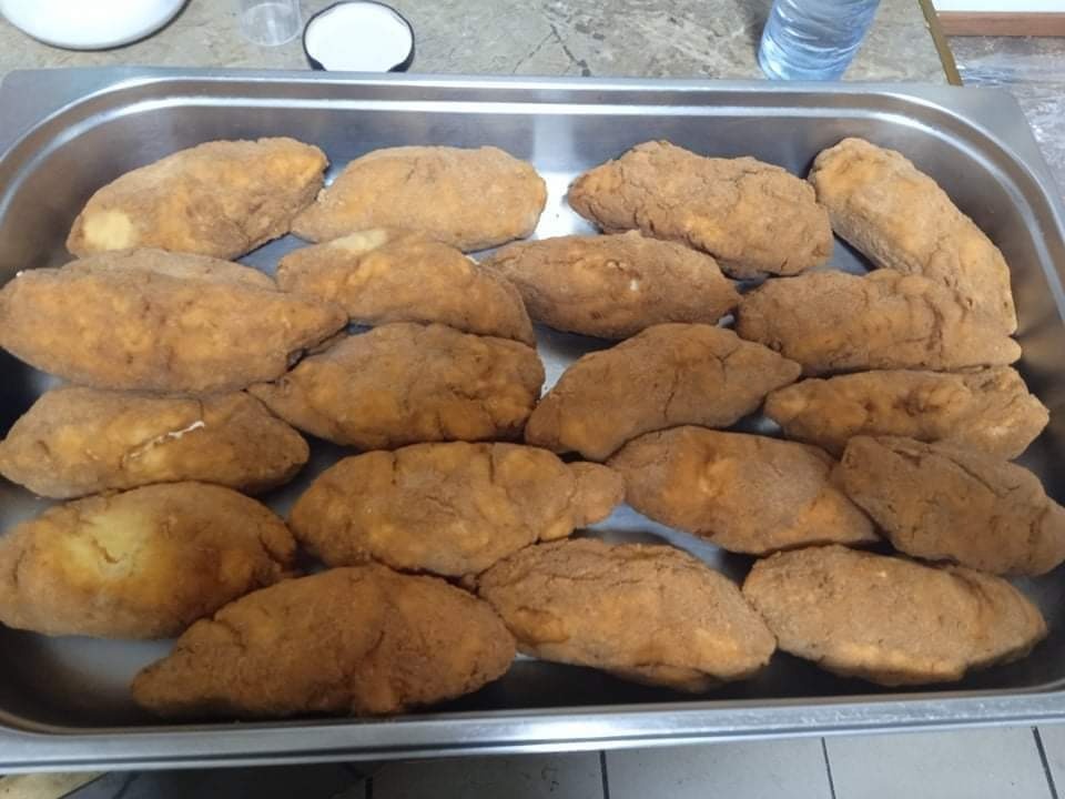 Metalowa taca wypełniona porcjami krokietów o nieregularnym kształcie i brązowawej panierce, widoczna butelka wody w tle.