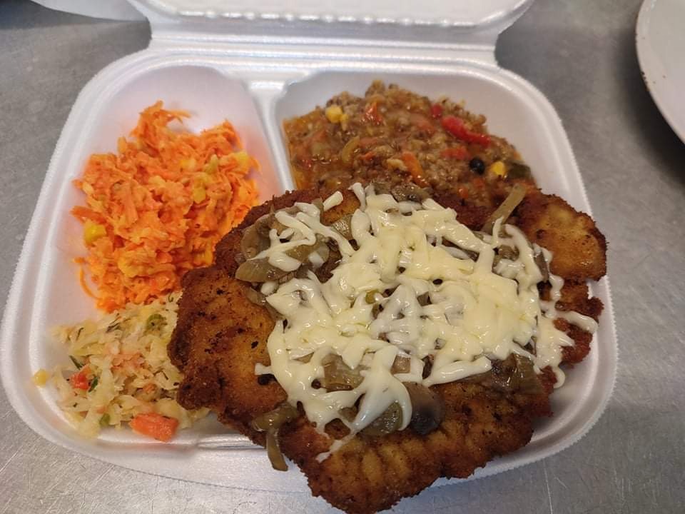 Porcja obiadowa w styropianowym pudełku: kotlet schabowy z serem i cebulą, surówka z marchwi i kukurydzy, oraz kasza z warzywami.