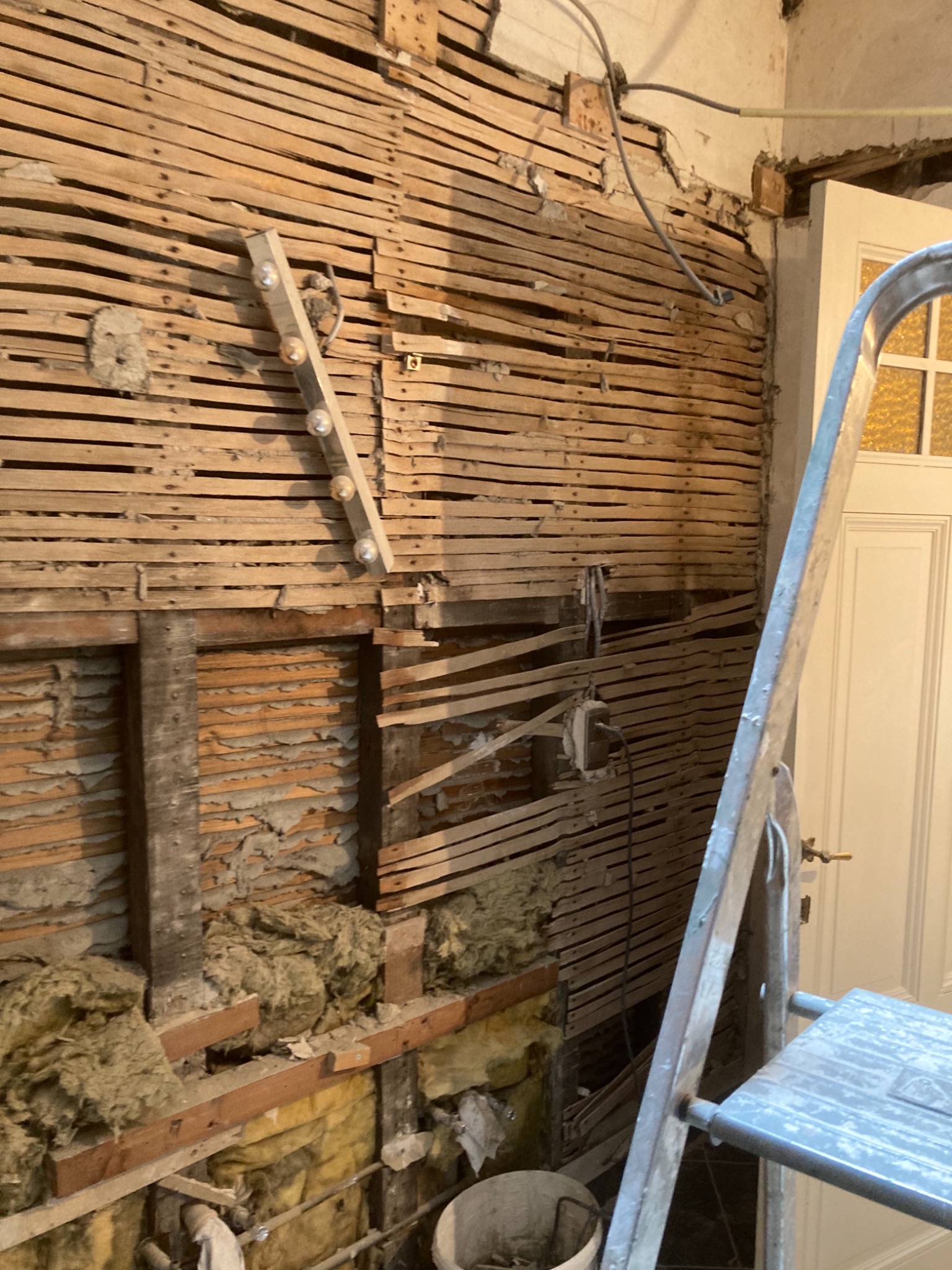 Ściana w trakcie remontu z odsłoniętą konstrukcją drewnianą i częściowo widoczną izolacją z wełny mineralnej, obok stoi drabina.