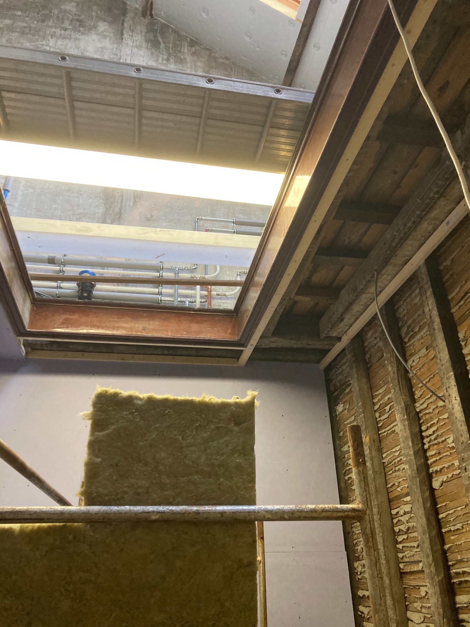 Montaż izolacji z wełny mineralnej na poddaszu w Nowogardzie, widoczne elementy konstrukcyjne dachu i instalacje.