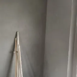 Świeżo otynkowane ściany w rogu pomieszczenia z widocznymi narzędziami: kielnią, szpachlą, miotłą i folią ochronną na podłodze.