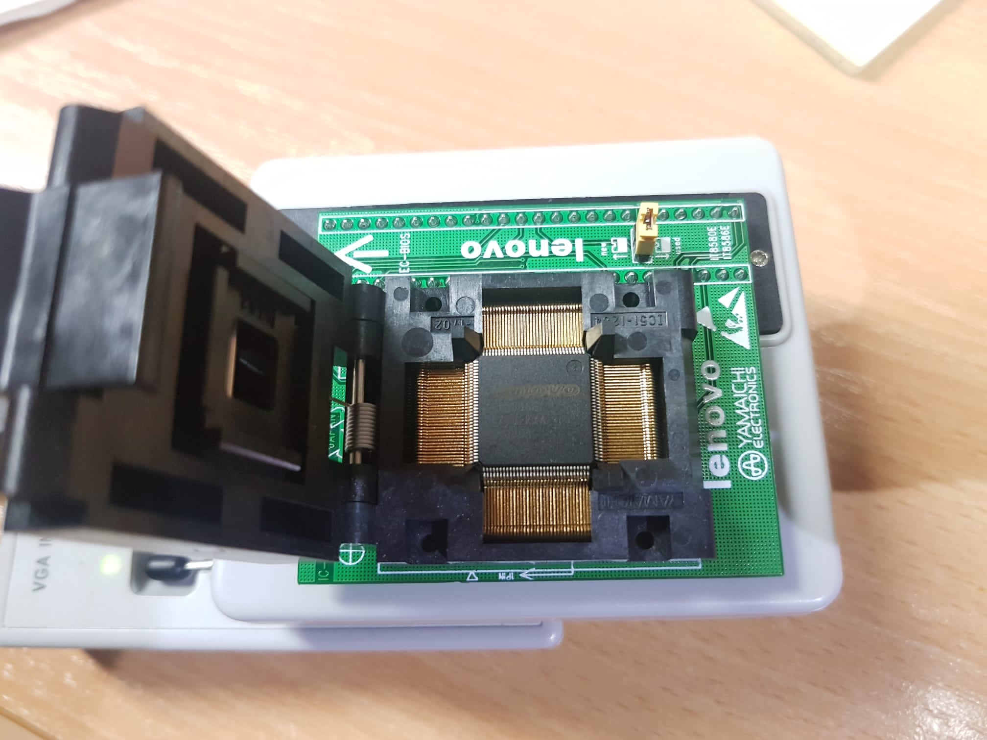 Programator układów scalonych z otwartą klapką, widoczna zielona płytka z elementami elektronicznymi i napisem Lenovo Yamachi Electronics.