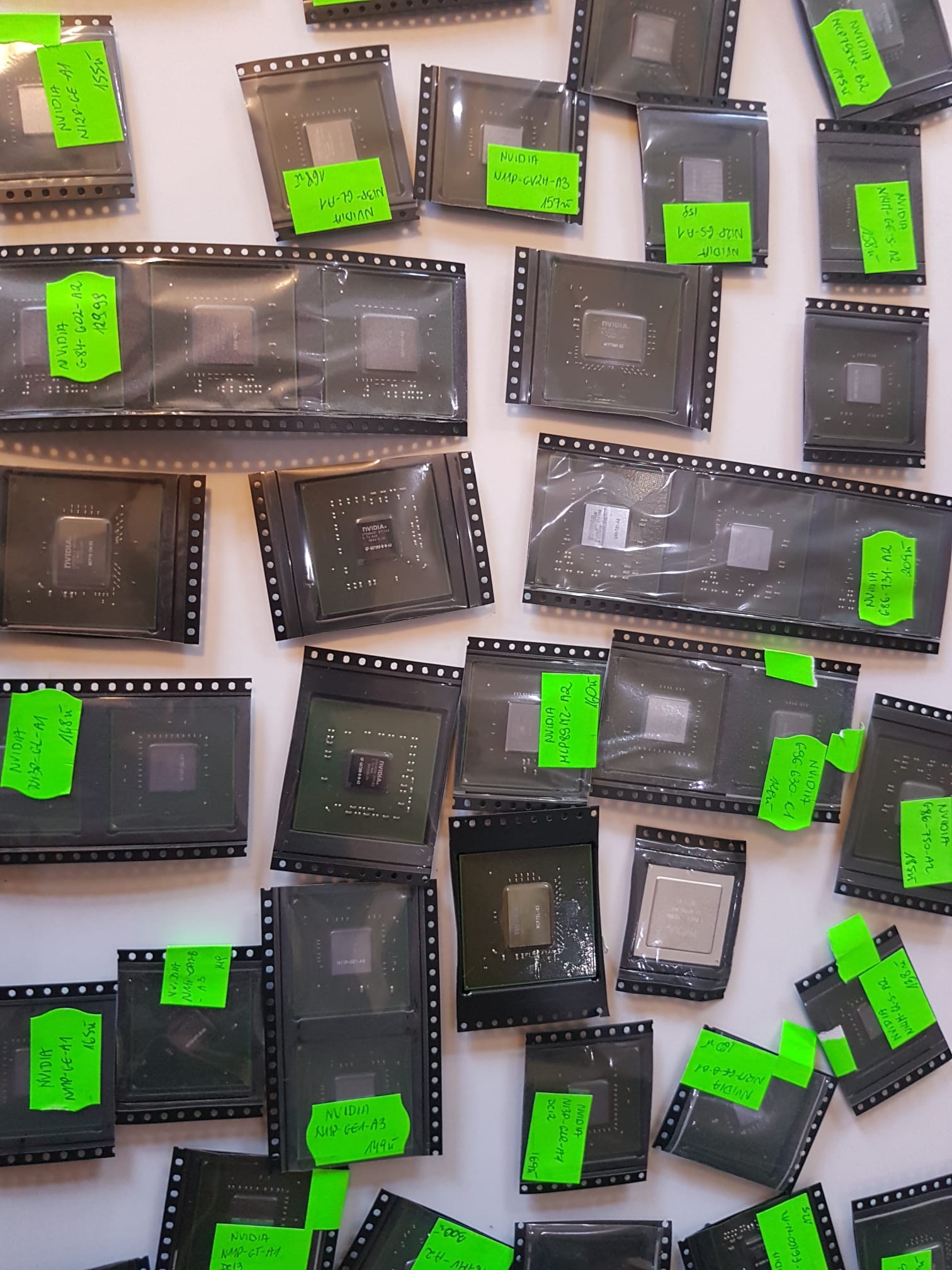 Zbliżenie na liczne układy scalone NVIDIA, każdy zapakowany w przezroczystą folię i oznaczony zieloną naklejką z modelem i ceną, rozłożone na białym tle w Krakowie. Widoczne różne modele, m.in.