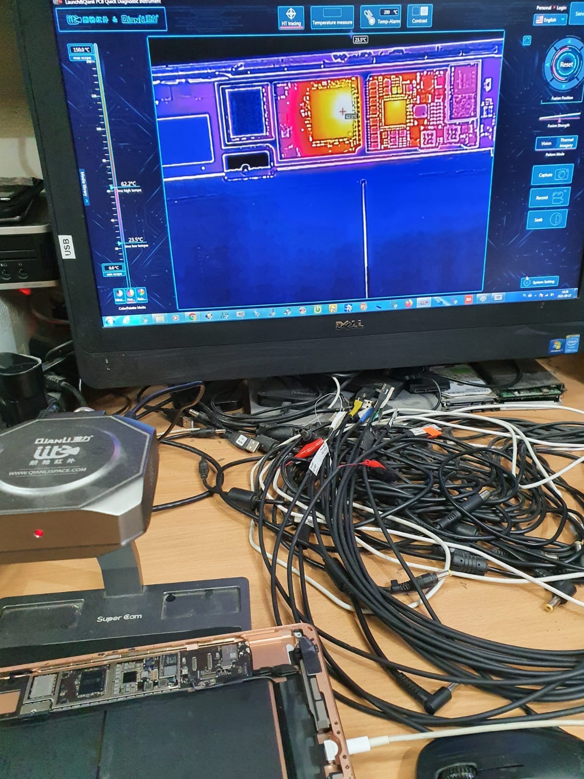 Diagnostyka termowizyjna uszkodzonego tabletu za pomocą kamery termowizyjnej Qianli, widok na monitorze przedstawia rozkład temperatur na płycie głównej, na stole plątanina kabli i narzędzi.