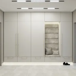 Szafa w przedpokoju z wnęką do siedzenia wykończoną tapicerowanym panelem ściennym i podświetleniem LED, uzupełniona poduszkami, z parą czarnych butów sportowych na podłodze.