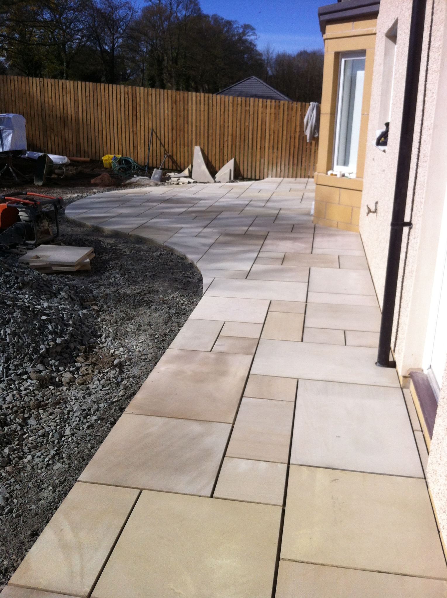 Świeżo ułożony, beżowy chodnik z płyt kamiennych o nieregularnym kształcie, obok gruz i narzędzia budowlane w słoneczny dzień.