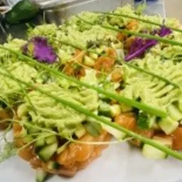 Porcje tatara z łososia z awokado, ogórkiem i szczypiorkiem na białych talerzach, przygotowane w kuchni cateringowej.