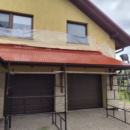 Complex-Dach Dawid Dębski - Przygotowania do malowania elewacji domu jednorodzinnego: okna zabezpieczone folią, rusztowanie rozstawione, dach pokryty nową, czerwoną blachą trapezową.