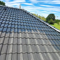 Complex-Dach Dawid Dębski - Częściowo umyty dach z szarej dachówki ceramicznej, ukazujący różnicę między czystą a brudną powierzchnią, na tle błękitnego nieba z chmurami.