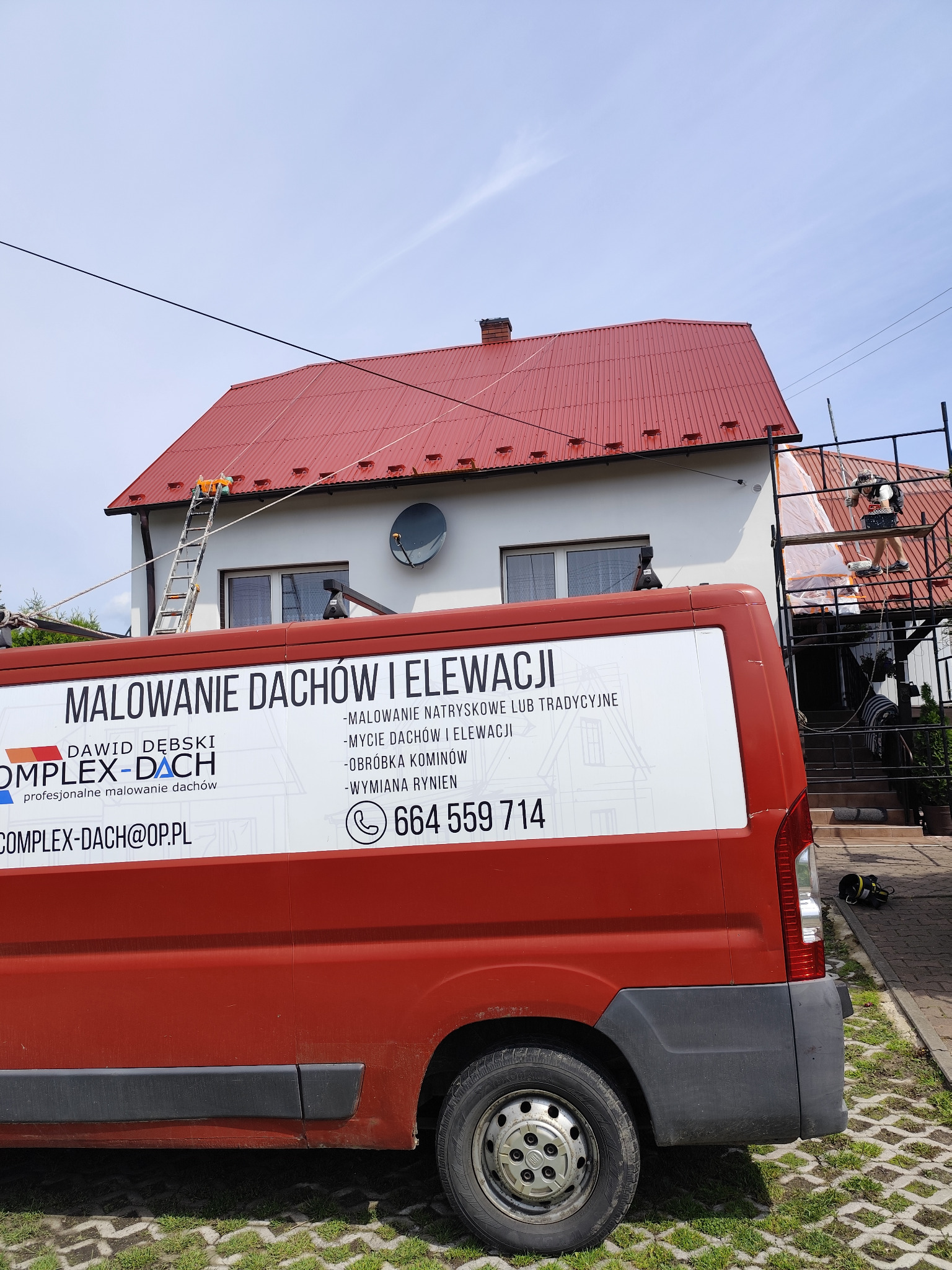 Czerwony bus firmy z Bachowic z reklamą usług malowania dachów i elewacji na tle domu z czerwonym dachem, gdzie ekipa pracuje na rusztowaniu i drabinie.