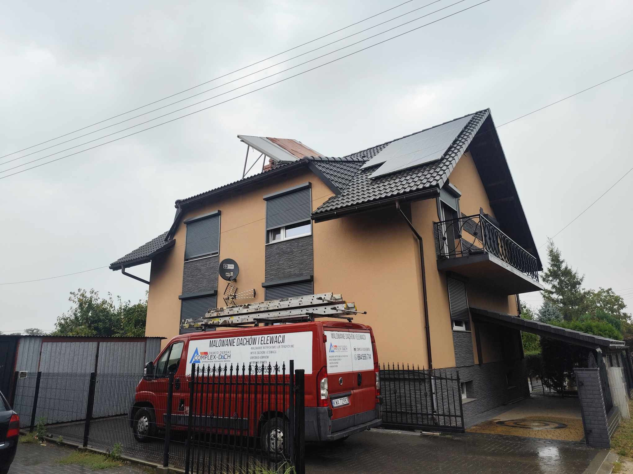 Ukończony remont domu jednorodzinnego z nową elewacją w odcieniach beżu i szarości, ciemnym dachem z panelami słonecznymi, widoczne rynny i obróbki blacharskie, na dachu antena satelitarna,...