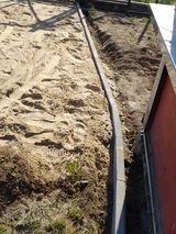 Ułożony krawężnik oddzielający piaskowe podłoże od ściany budynku, widoczne ślady prac ziemnych.